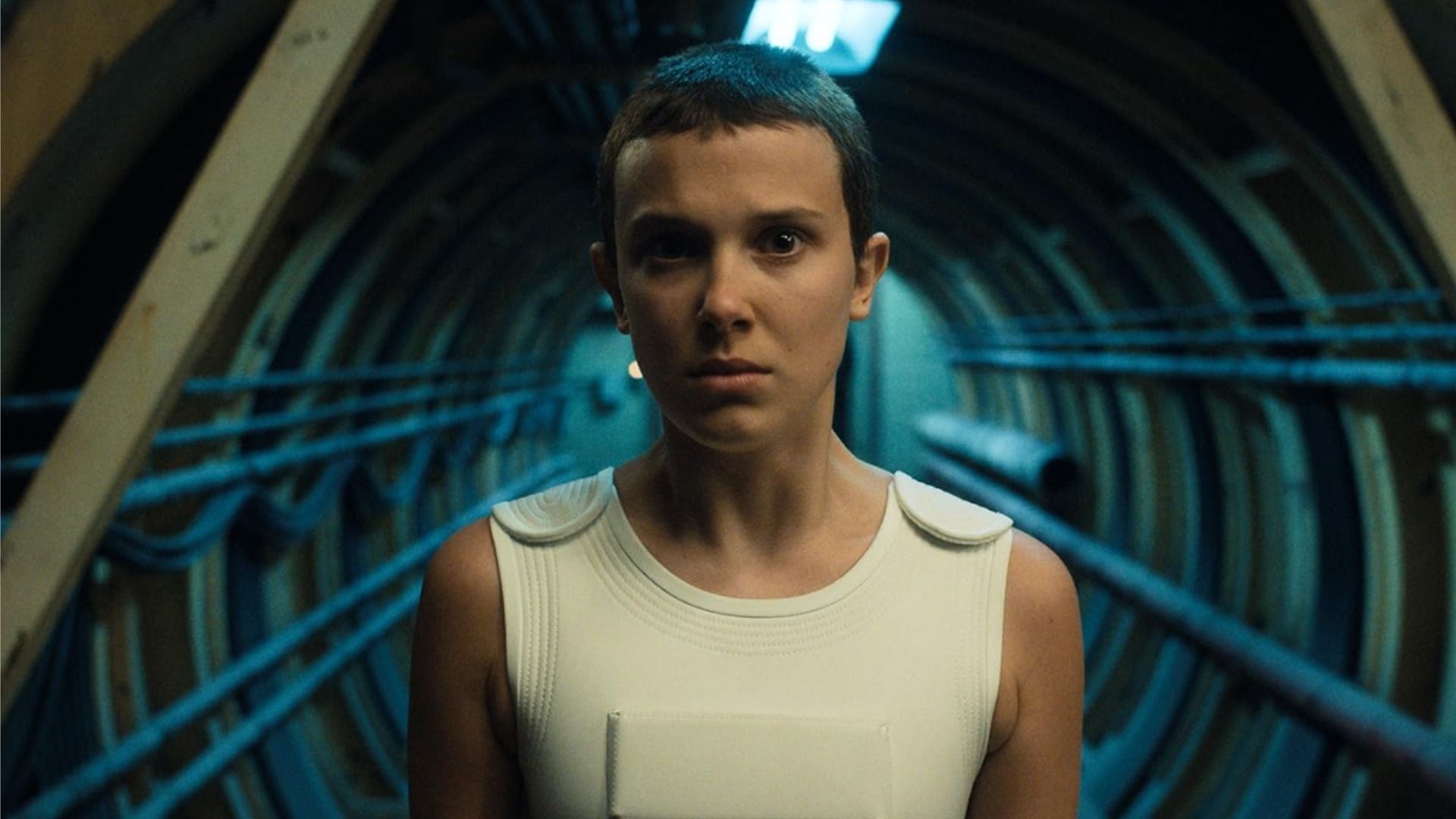 Millie Bobby Brown con un corte de pelo corto está de pie en un túnel mirando a la cámara