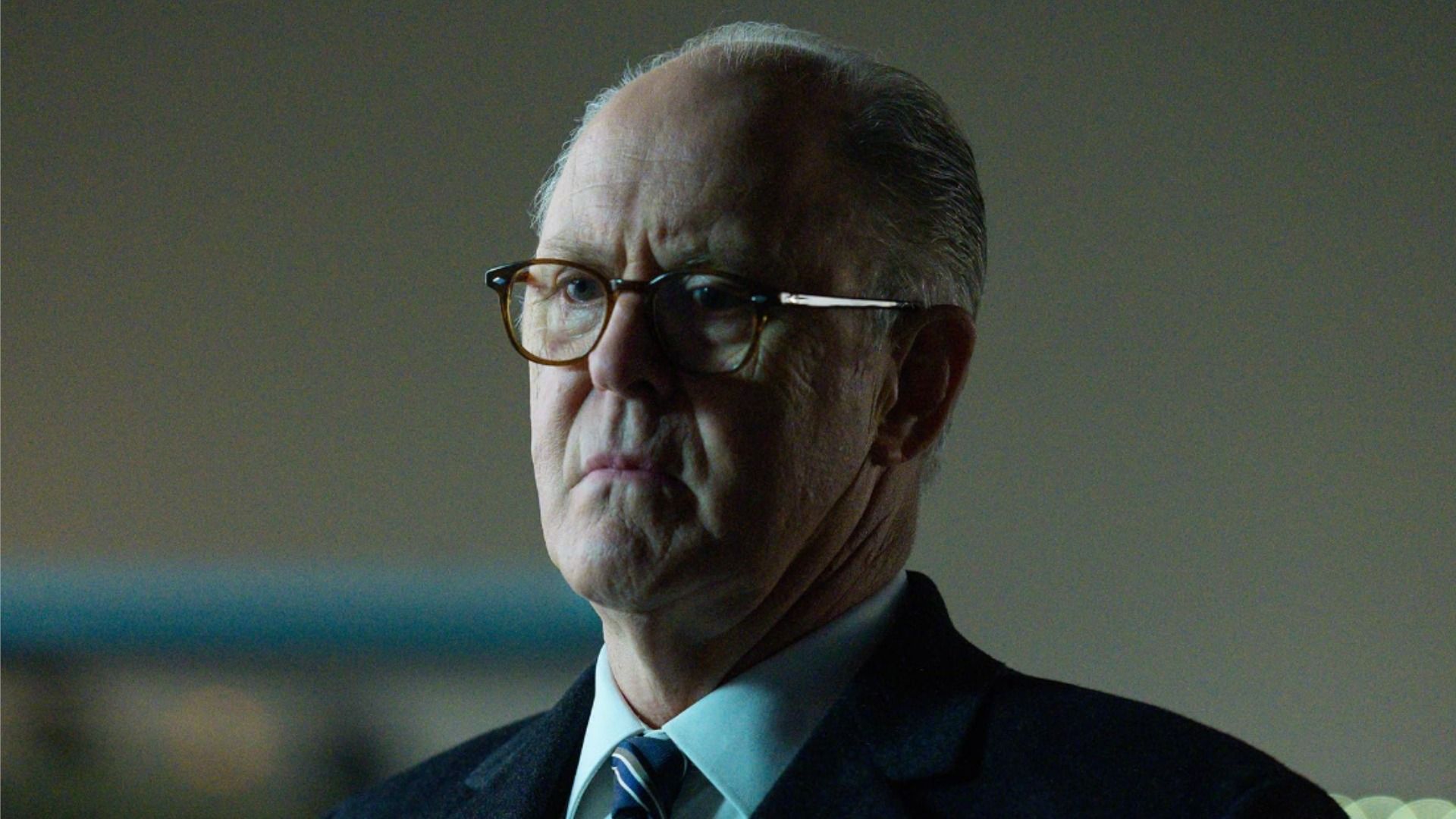 El actor John Lithgow con gafas y una chaqueta negra mira hacia un lado
