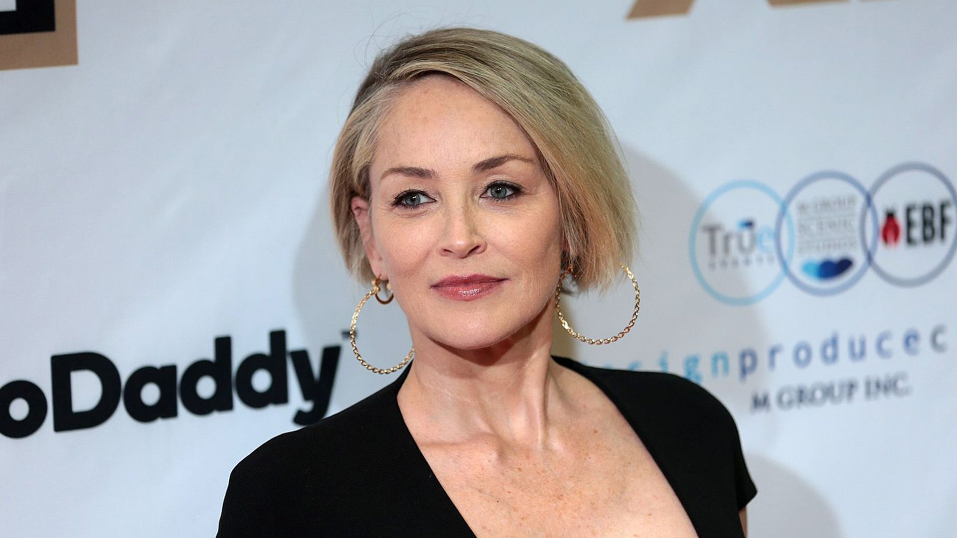 Actriz Sharon Stone con corte de cabello bob, pendientes de aro dorados y vestido negro
