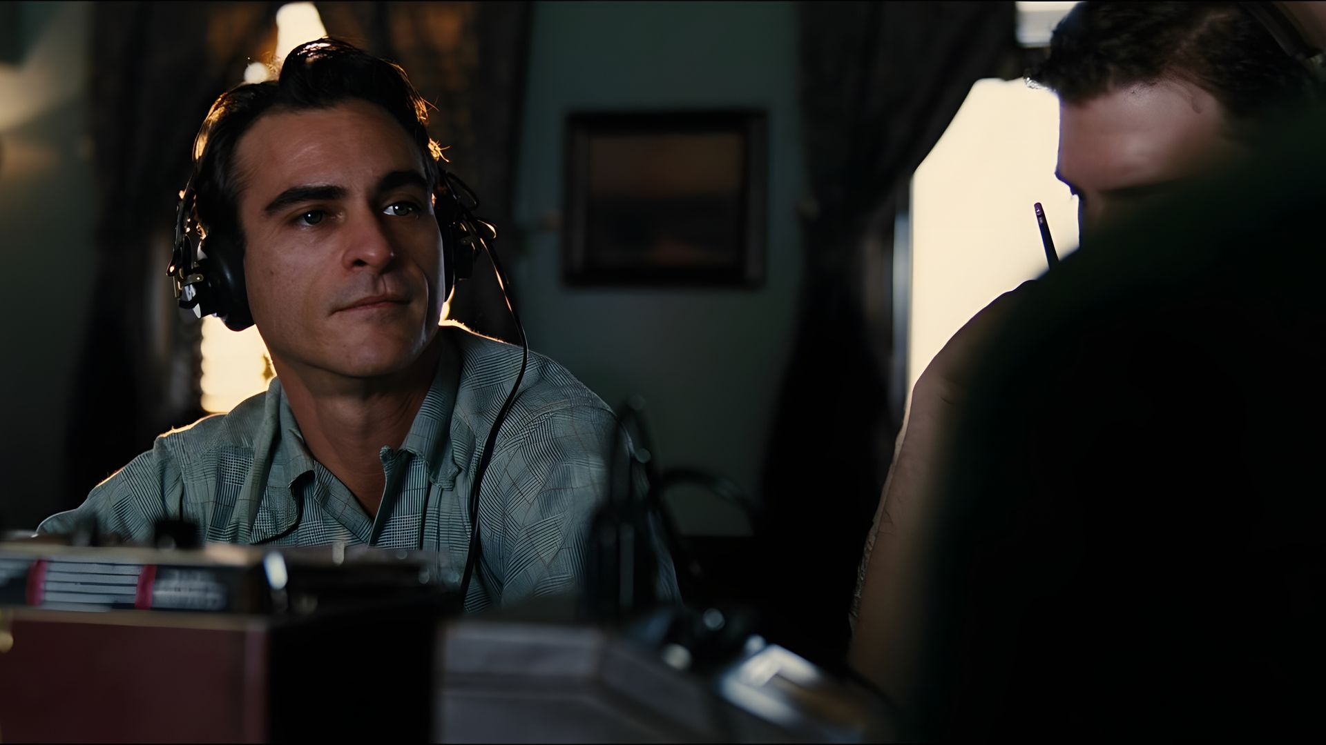 Joaquin Phoenix con una camisa azul y grandes auriculares mira a la distancia