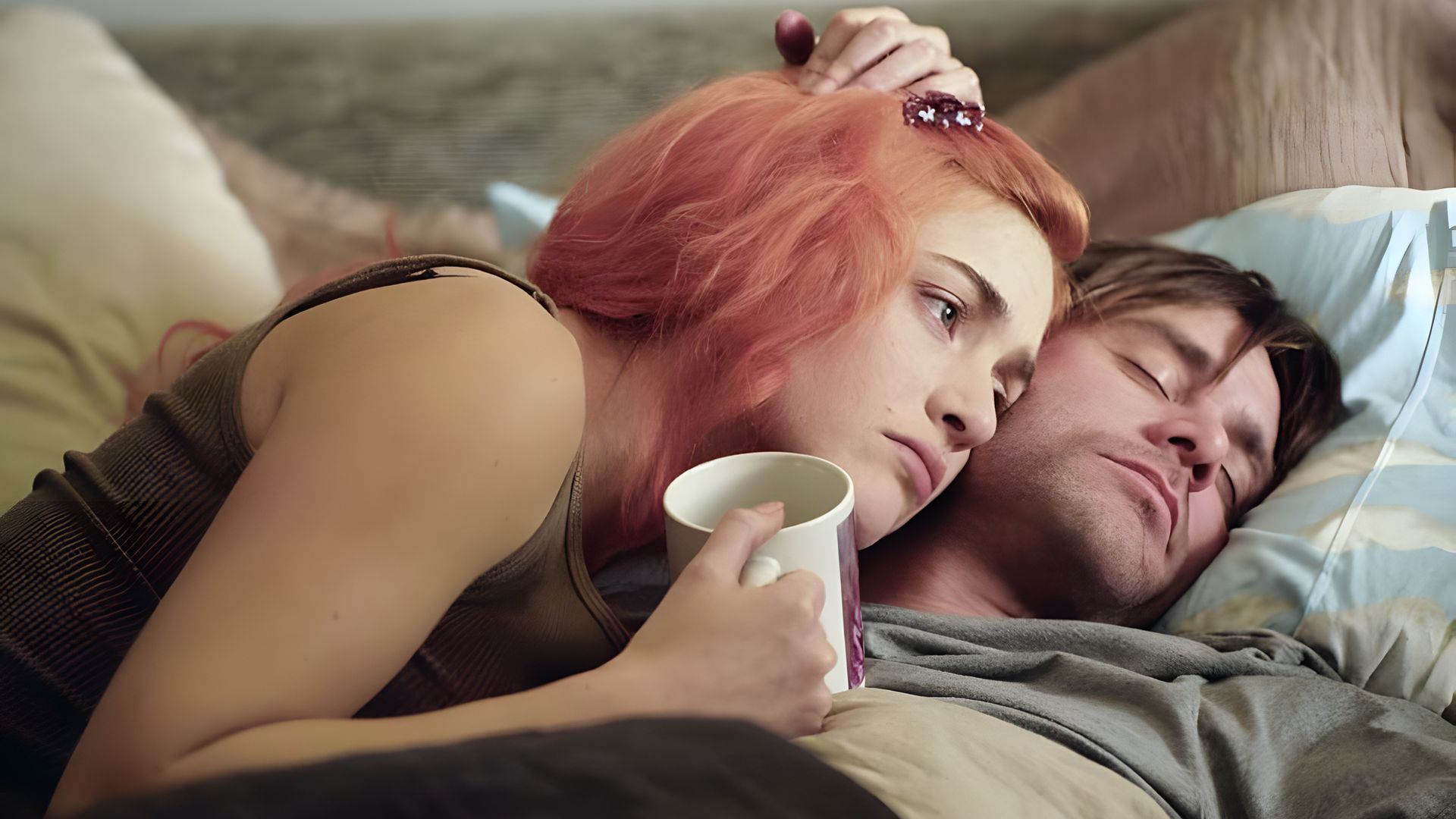 Una mujer con el pelo rosa yace junto a un hombre dormido, abrazándolo y sosteniendo una taza en su mano, mirando pensativamente a lo lejos.