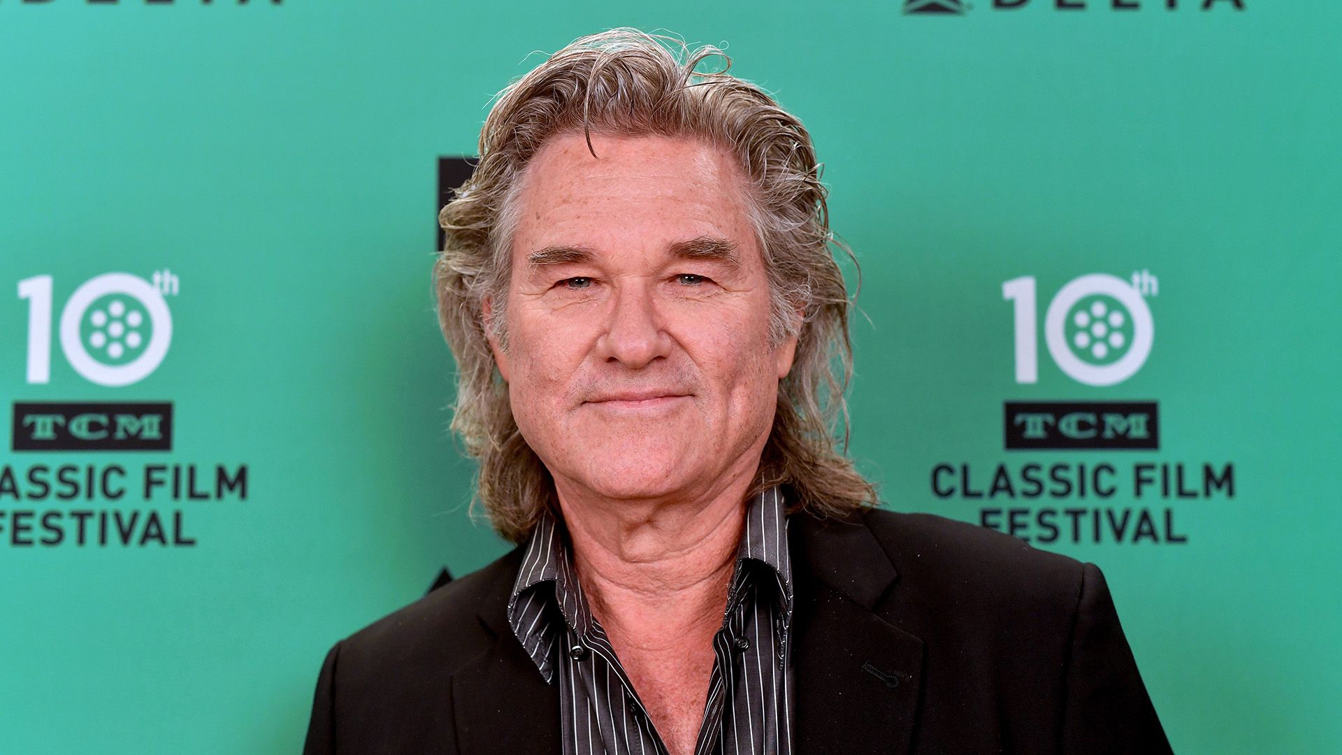 Actor Kurt Russell con cabello largo y gris sobre un fondo turquesa