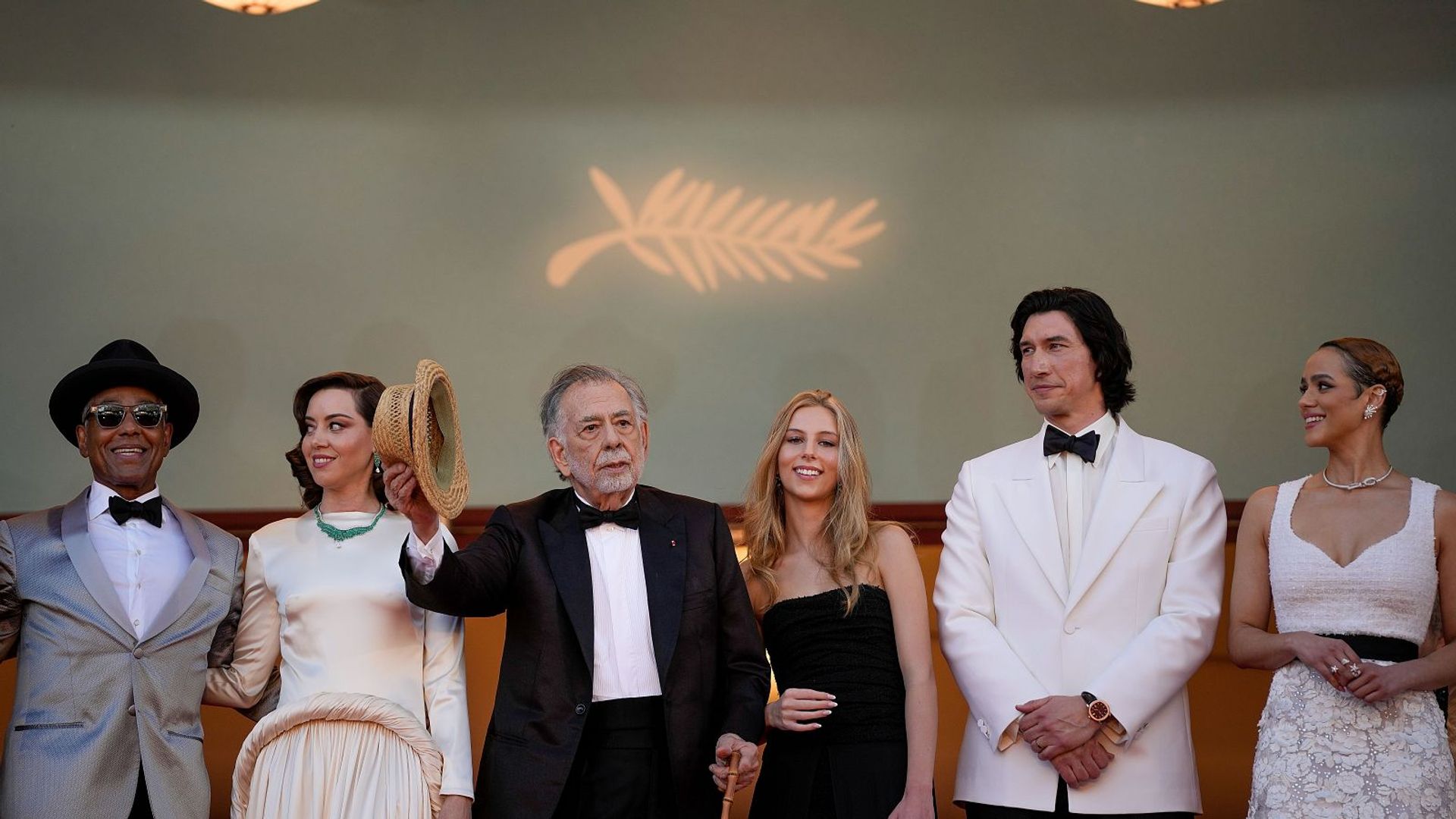 Un grupo de personas elegantemente vestidas posa en la alfombra roja del Festival de Cannes, con el fondo de la palma de oro.