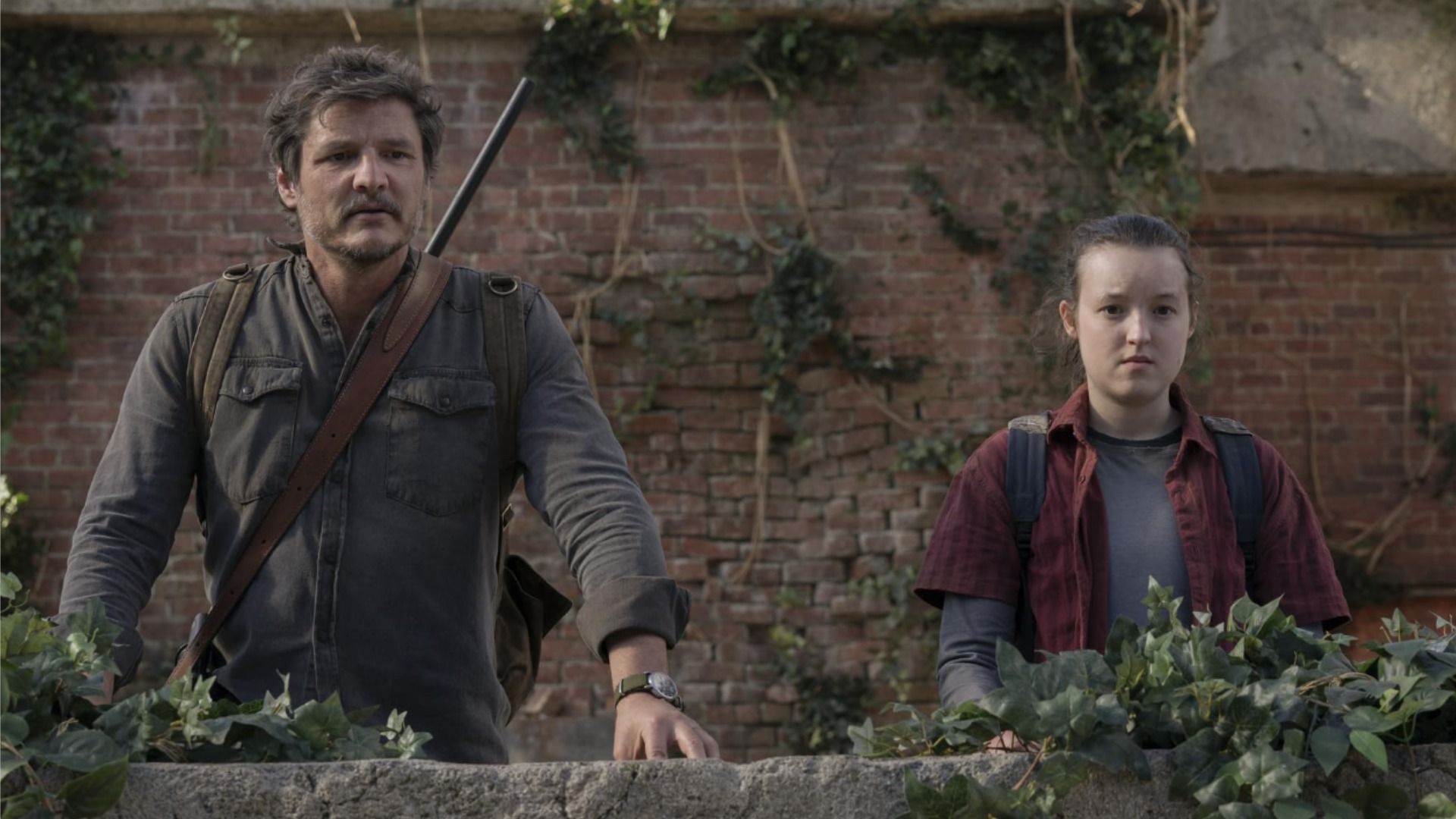 Actores Pedro Pascal y Bella Ramsey de pie sobre el techo de una casa contra una pared de ladrillo