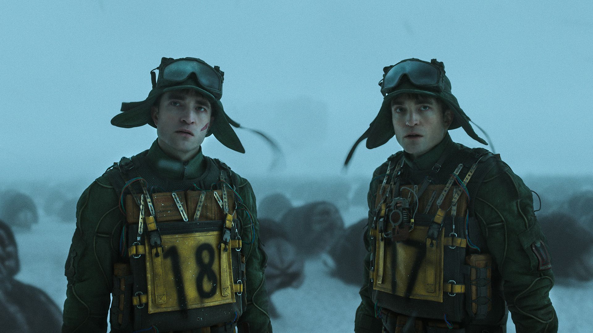 Dos Robert Pattinson idénticos están uno al lado del otro, ambos con sombreros y gafas protectoras, uno con el número 18 en el pecho, el otro 17