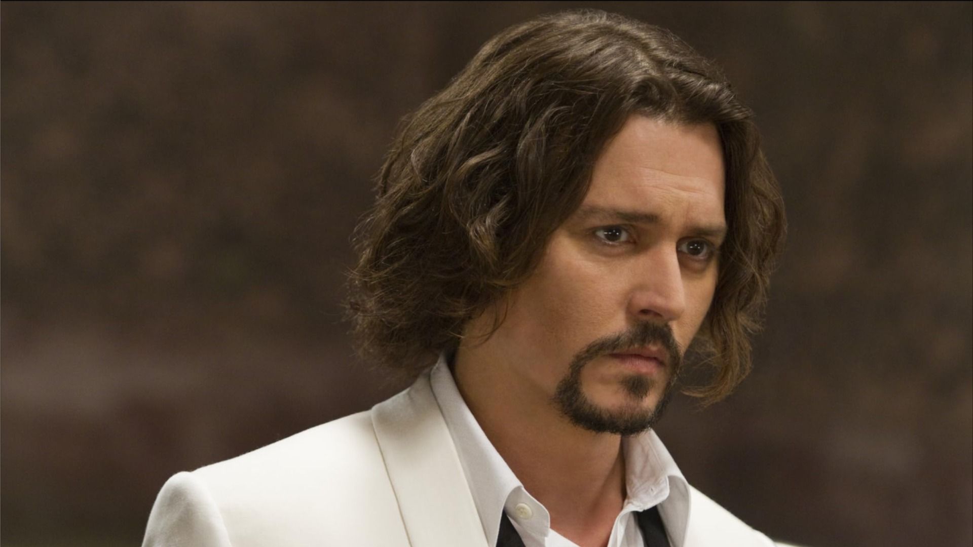 Actor Johnny Depp in a white jacket and with long hair looks to the side