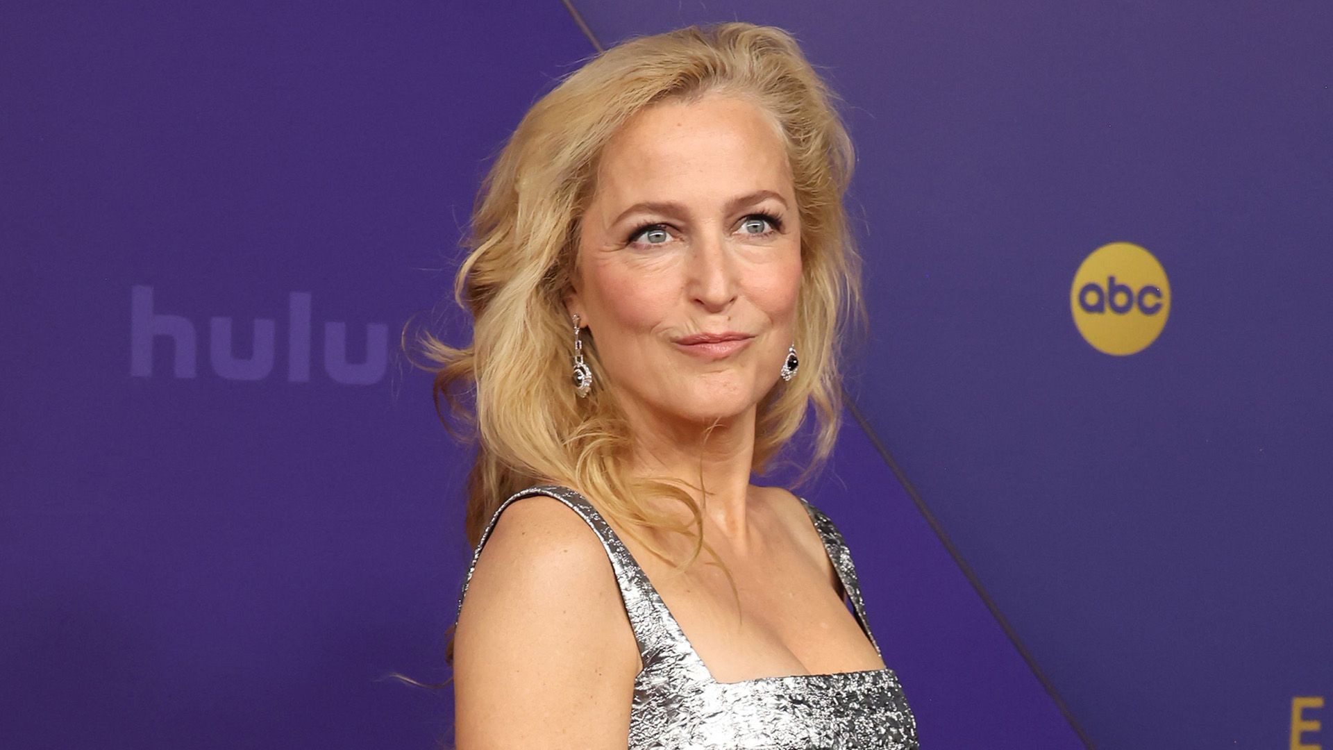 Actriz Gillian Anderson en un vestido plateado contra un fondo púrpura