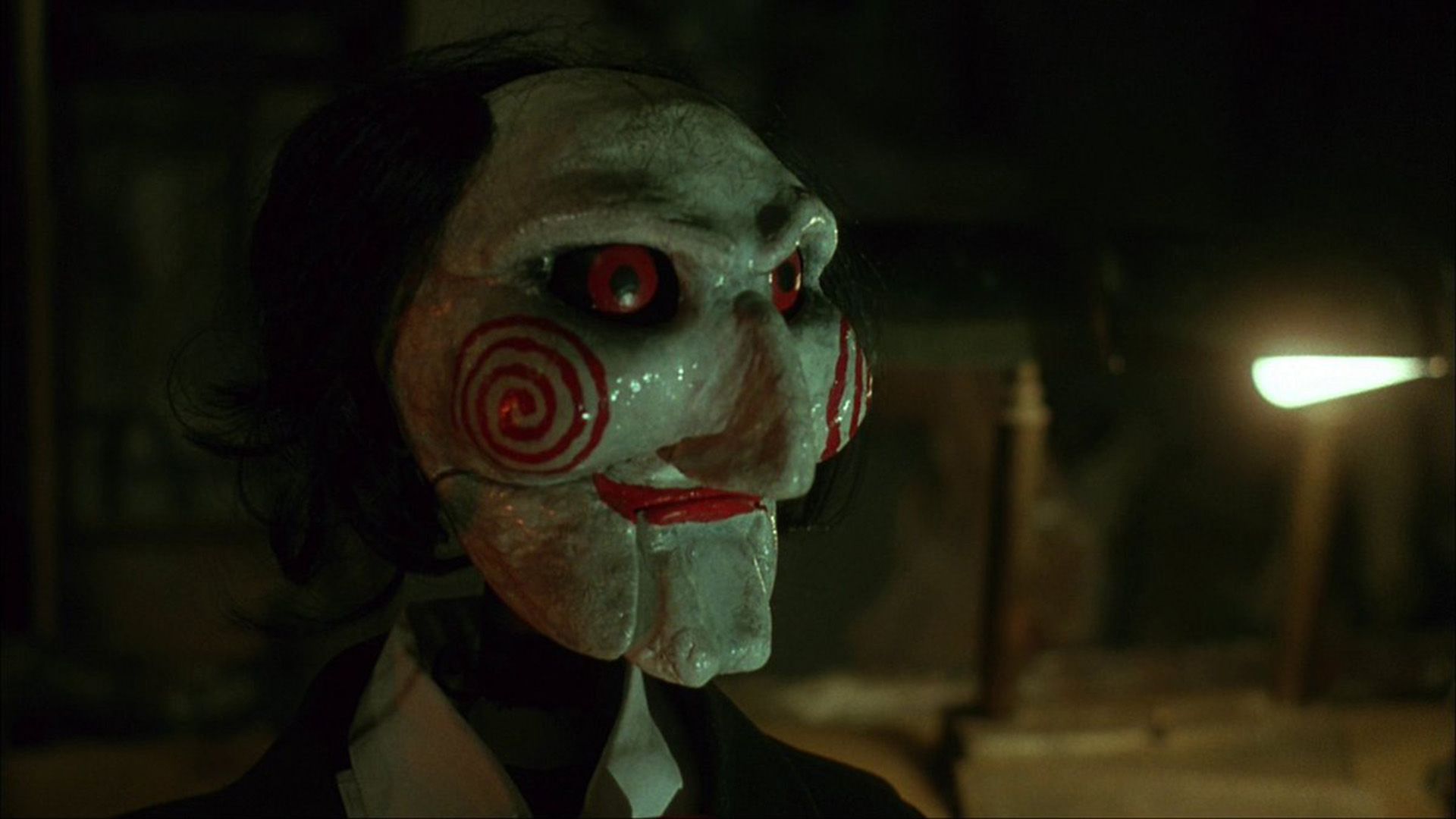 Muñeco espeluznante con cara blanca, ojos rojos y espirales rojas en las mejillas de la película 'Saw'