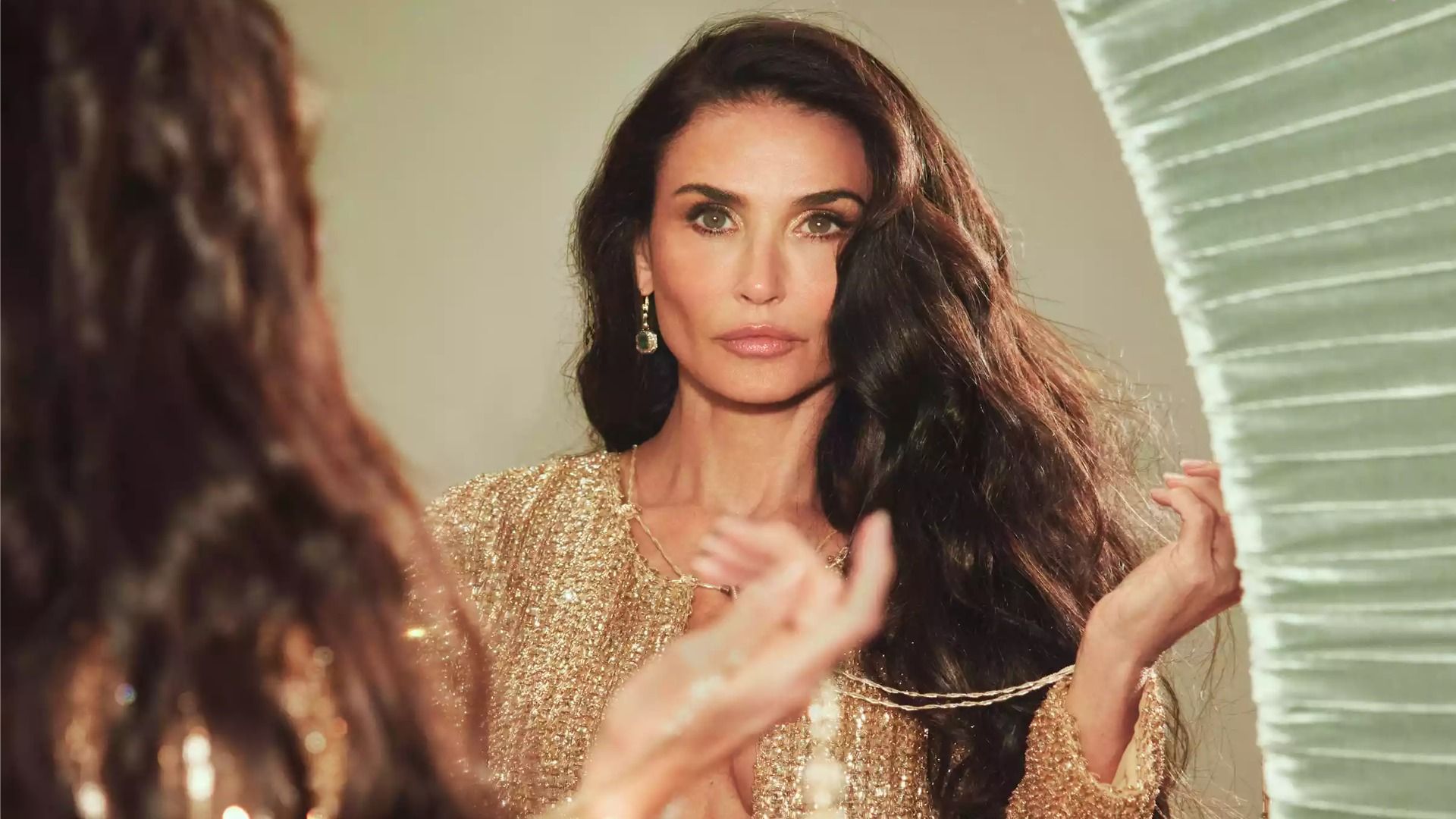 La actriz Demi Moore se encuentra frente a un espejo con un vestido dorado y se mira a sí misma en el reflejo