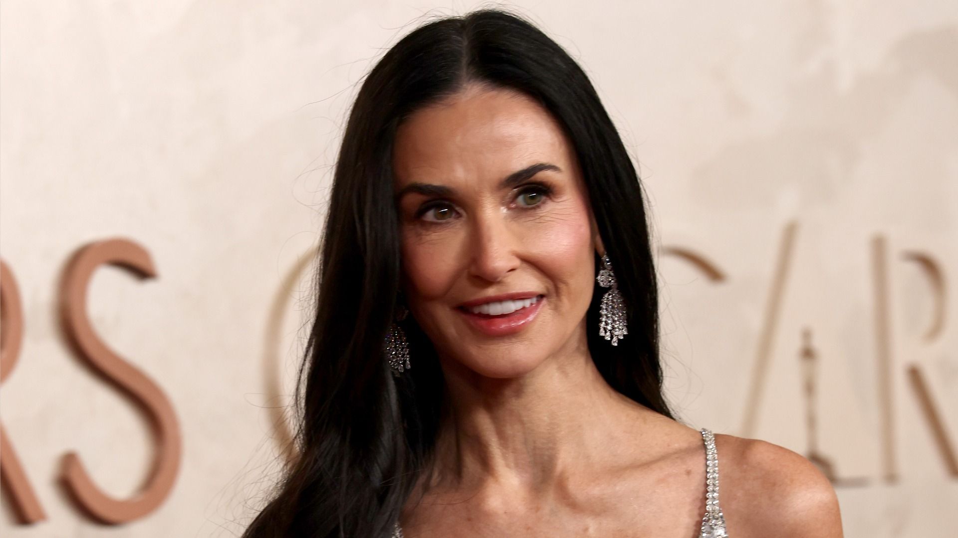 Actress Demi Moore looks to the side and smiles against a beige background with the inscription 'Oscar'