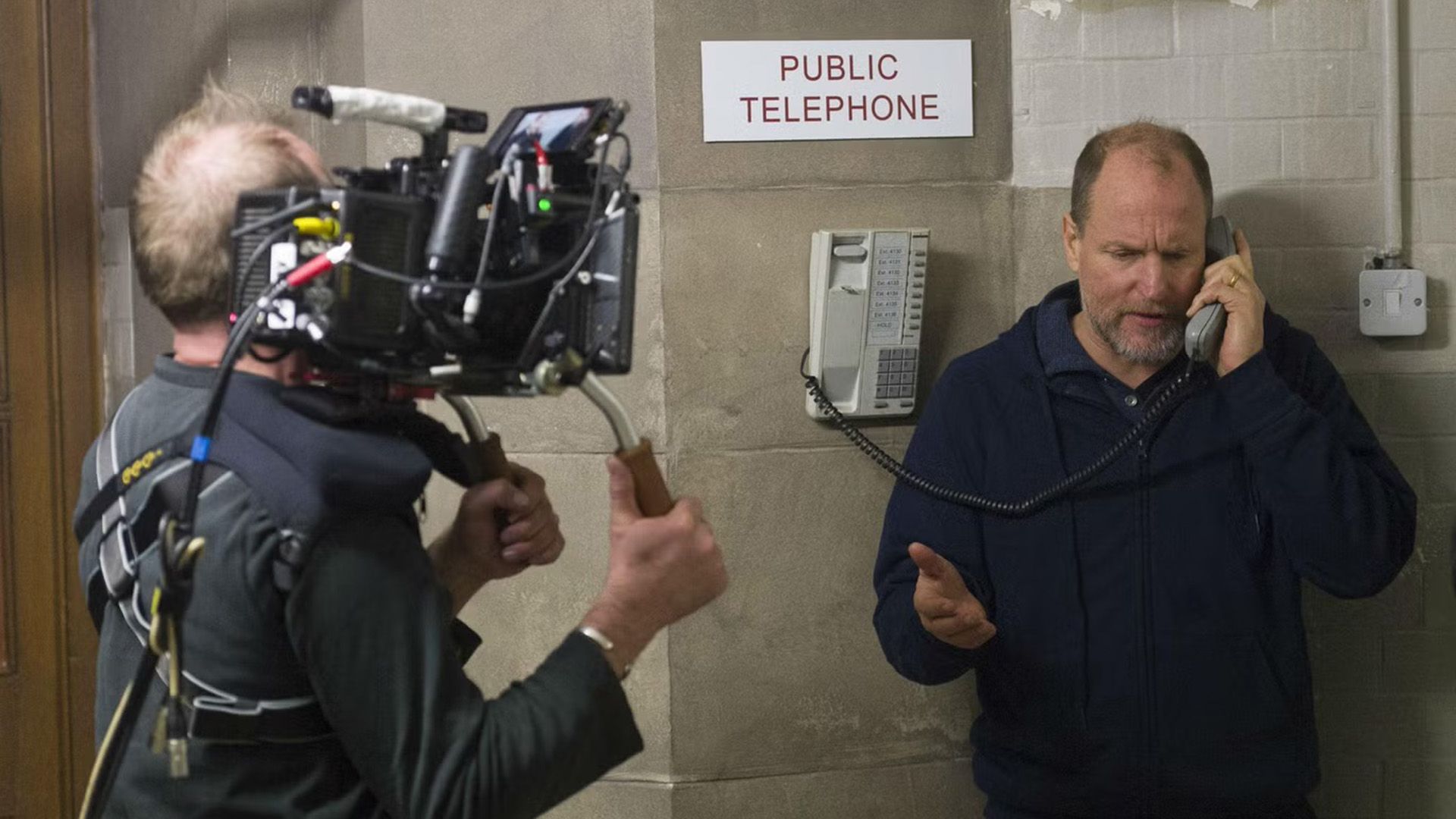 Woody Harrelson hablando por un teléfono público mientras es filmado por un camarógrafo