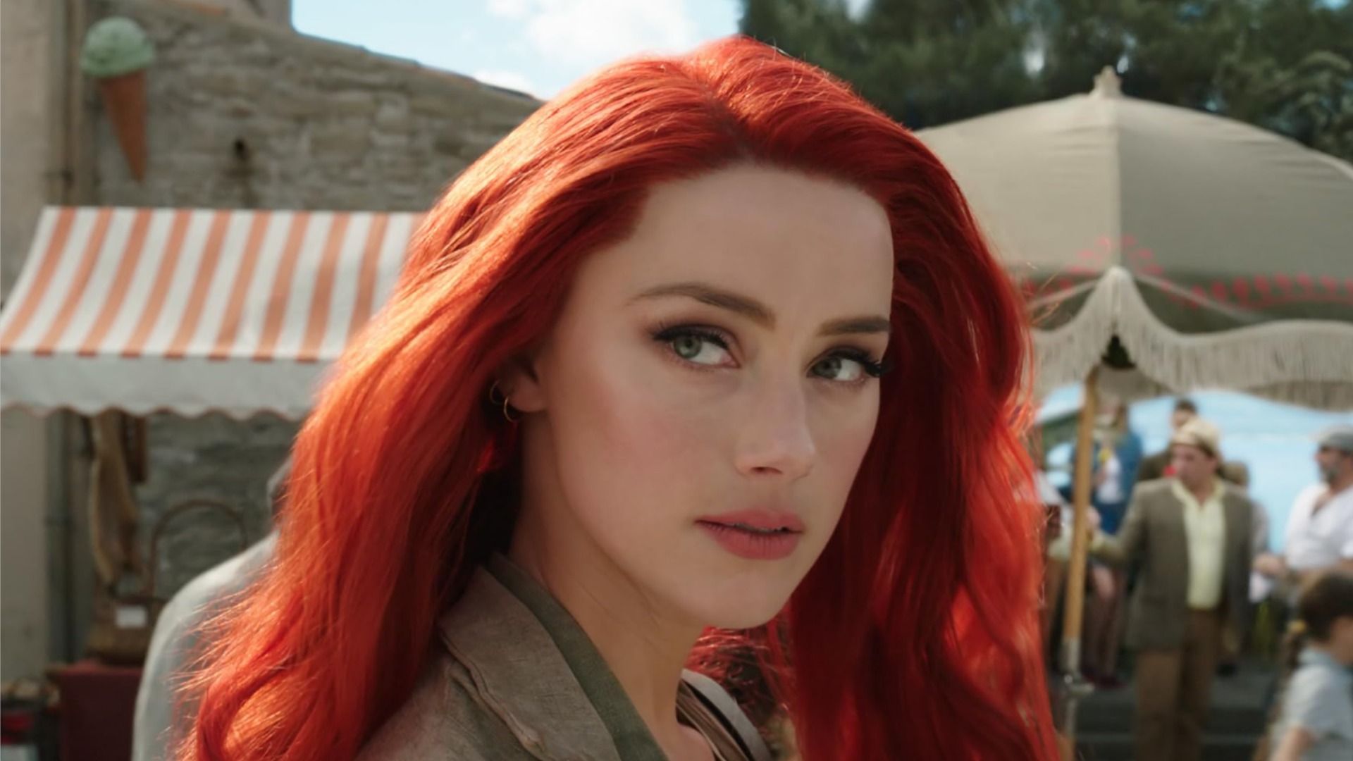 La actriz Amber Heard con cabello rojo mira de lado contra el fondo de la calle y la gente