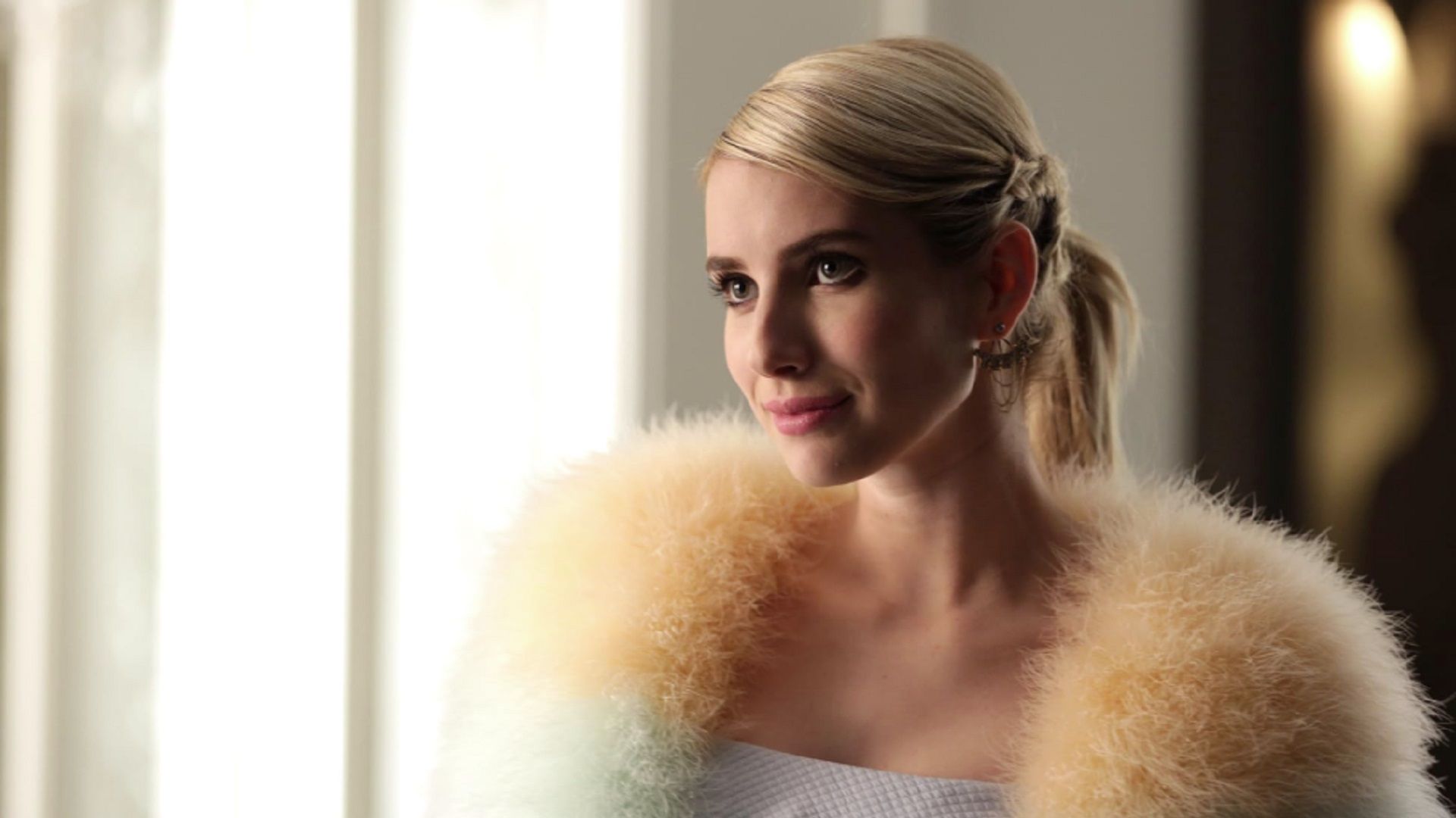Emma Roberts en una capa de piel mira dulcemente a la izquierda