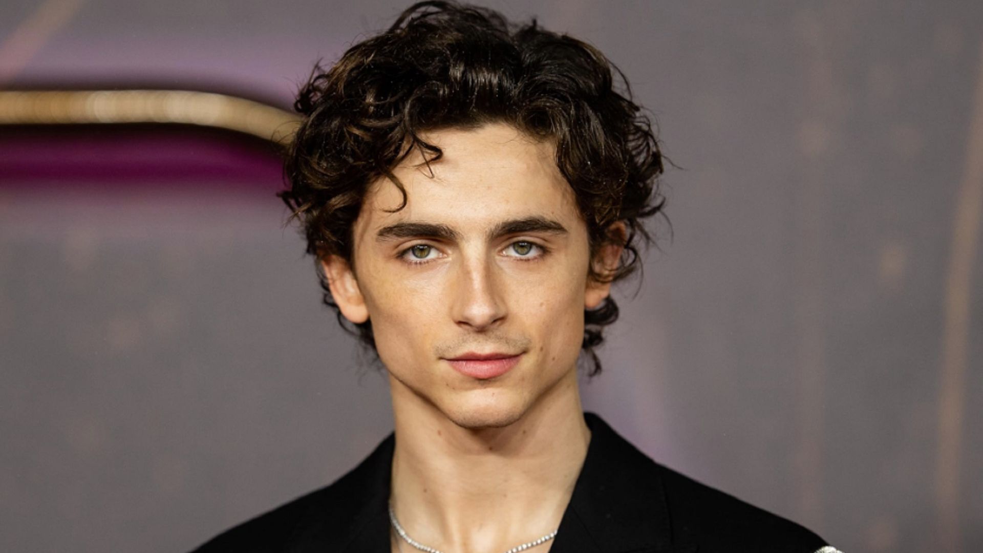 Timothée Chalamet in a black suit looks into the frame