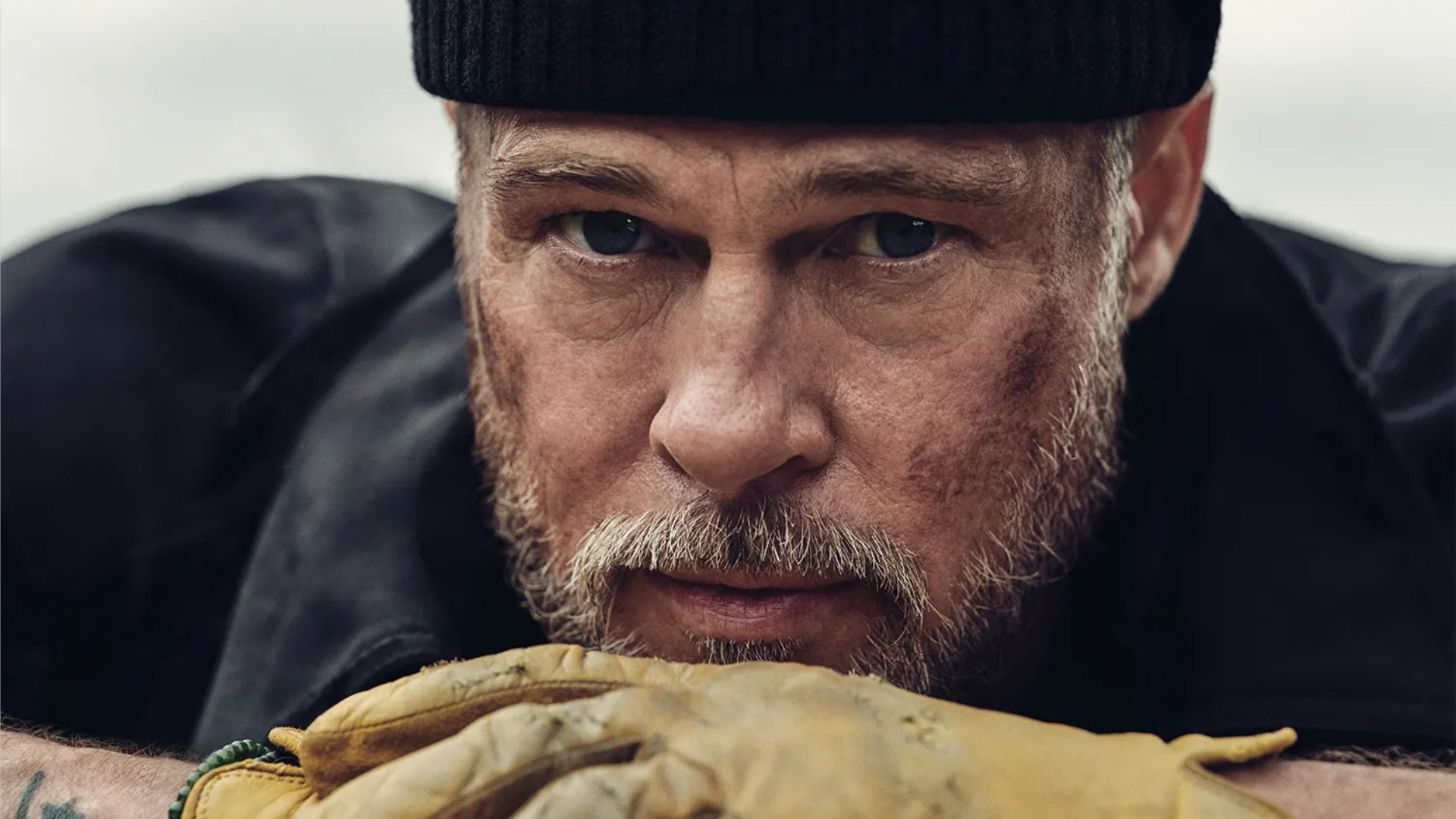 Actor Brad Pitt con un sombrero negro y guantes amarillos mirando a la cámara