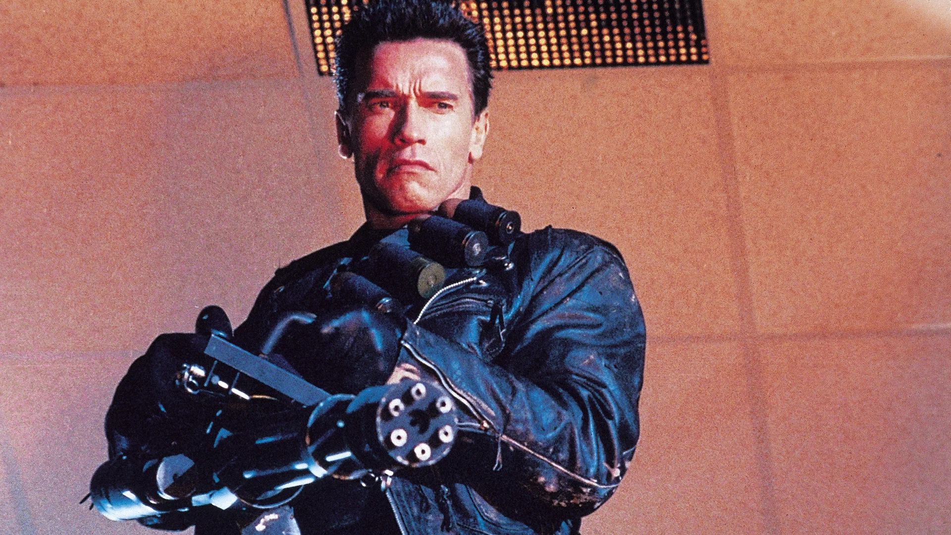 Arnold Schwarzenegger con una chaqueta de cuero negra sosteniendo una minigun