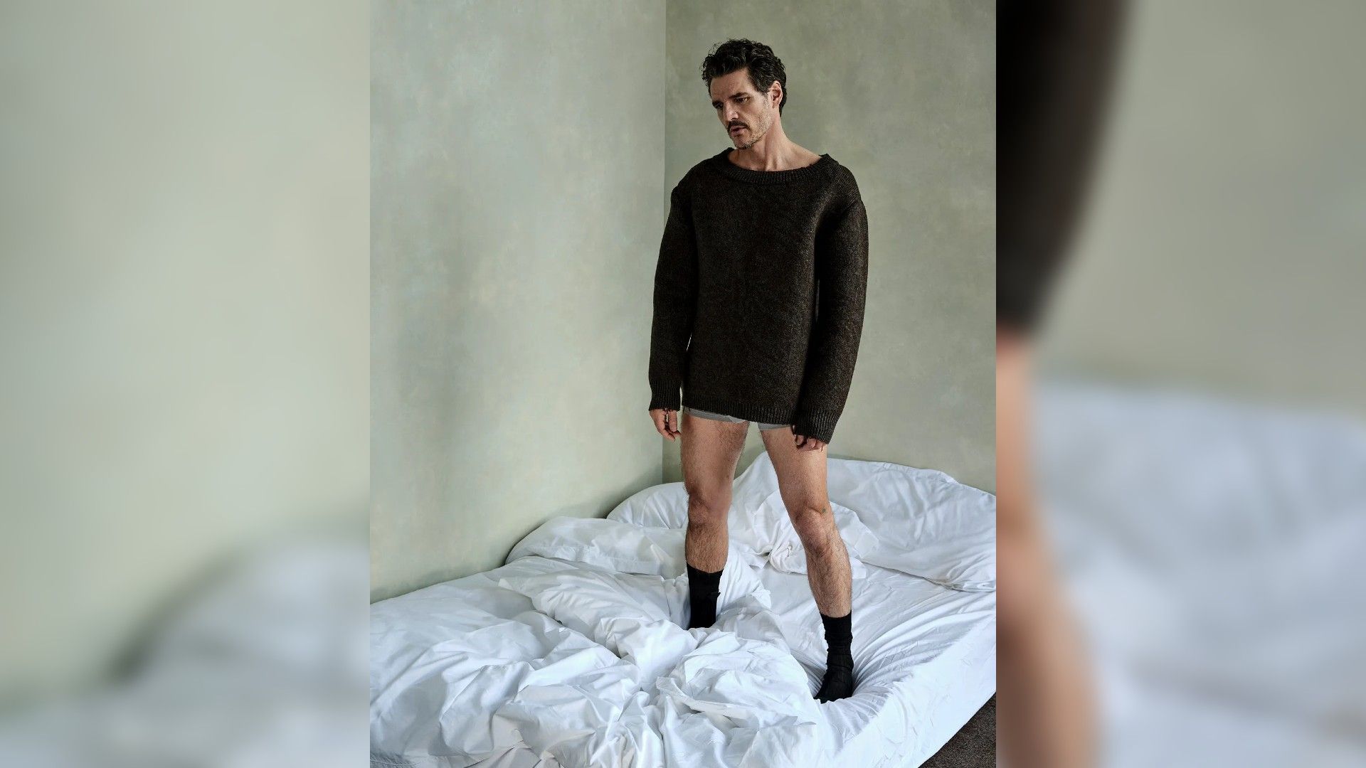 Pedro Pascal de pie en una cama con suéter y ropa interior