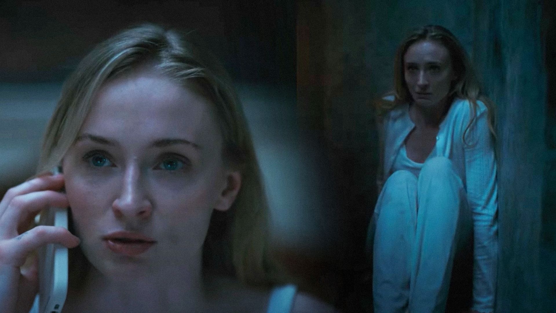 Actriz Sophie Turner con un teléfono en la mano sentada contra la pared en camisón