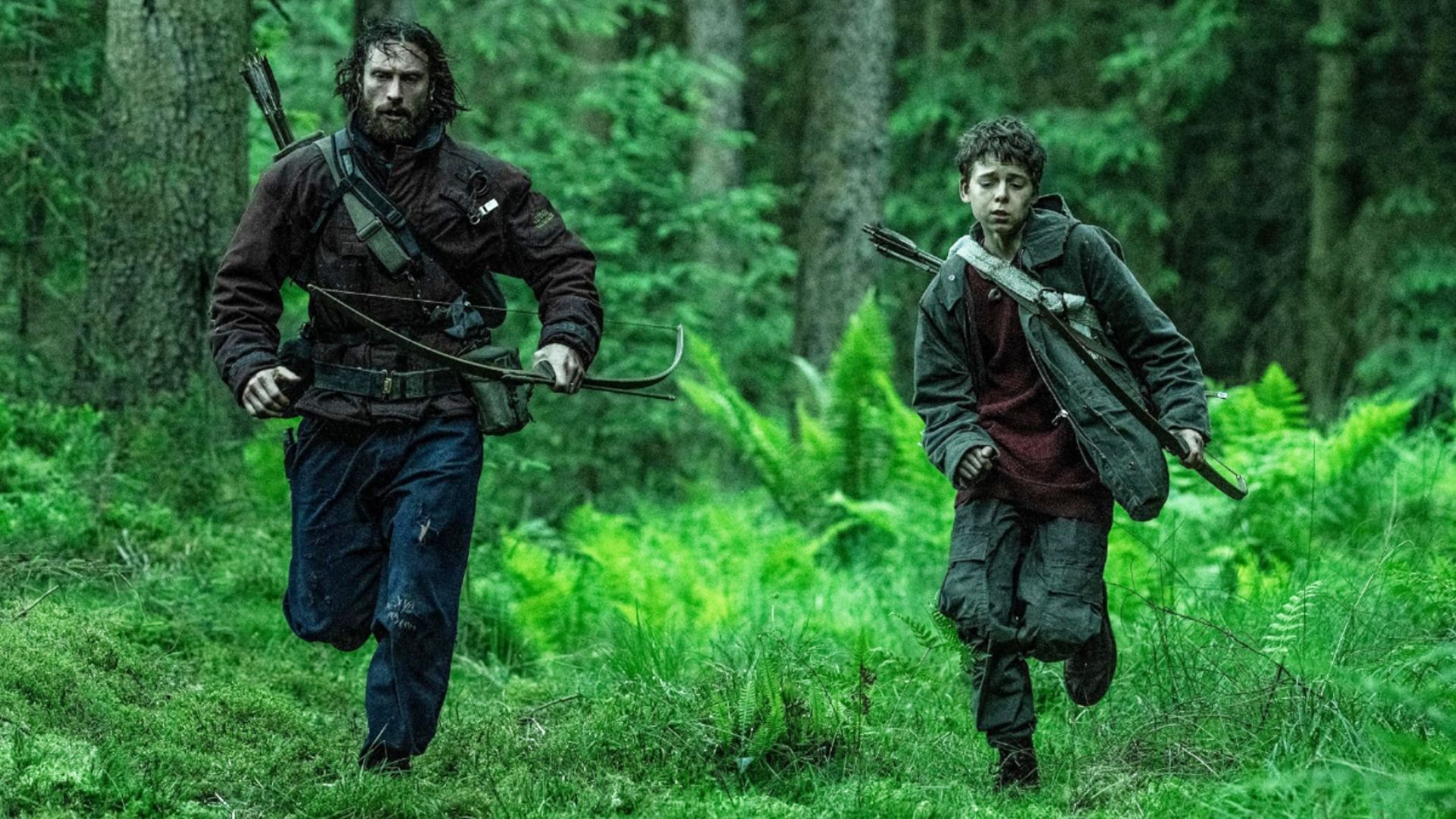 El actor Aaron Taylor-Johnson con ropa sucia corre por el bosque junto a un niño con arco