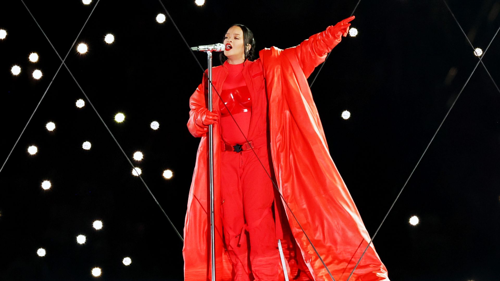 Rihanna con un traje rojo brillante y una capa larga actúa en el escenario con un micrófono