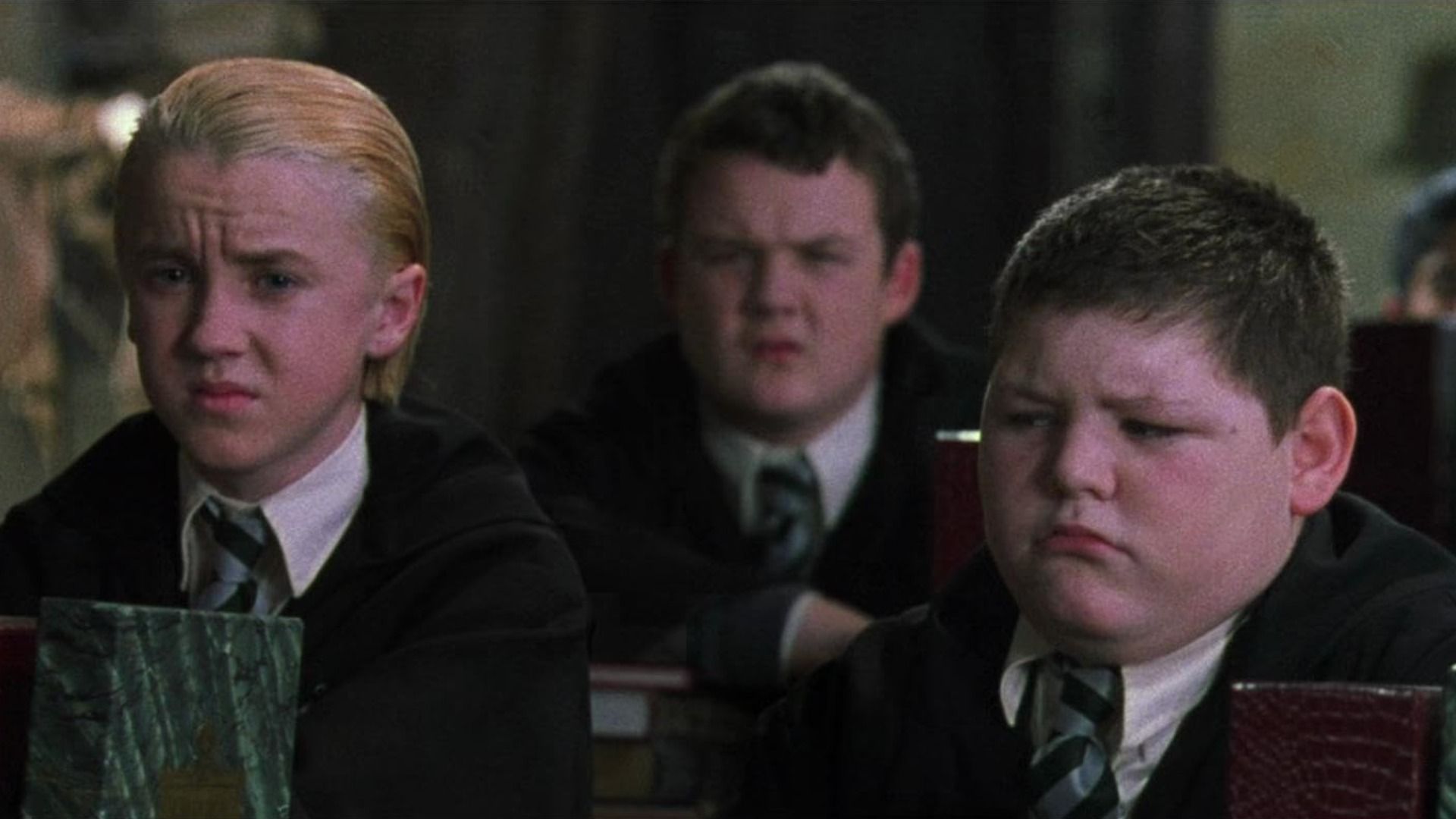 El actor Tom Felton en uniforme escolar sentado junto a dos chicos
