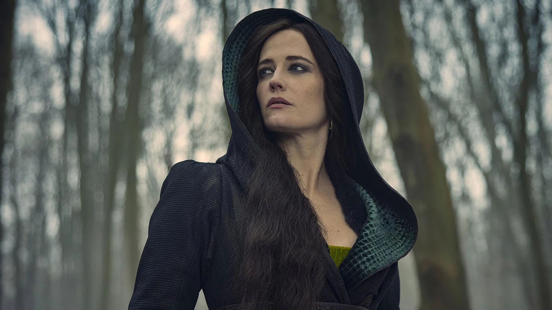 Eva Green con un vestido negro con capucha contra un fondo de bosque invernal