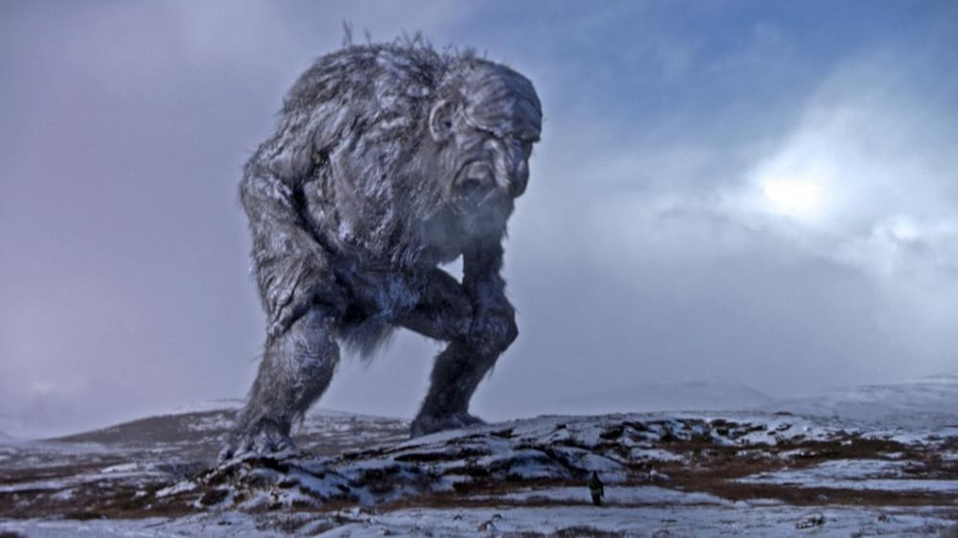 Un monstruo humanoide gris y masivo se alza sobre una carretera cubierta de nieve